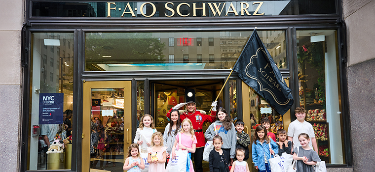 A group of children standing with a person dressed as a toy soldier in front of FAO Schwarz in New York City. 