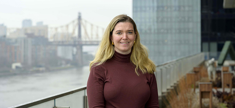 Meredith standing on an outdoor terrace with the 59th Street Bridge in New York City behind her.  